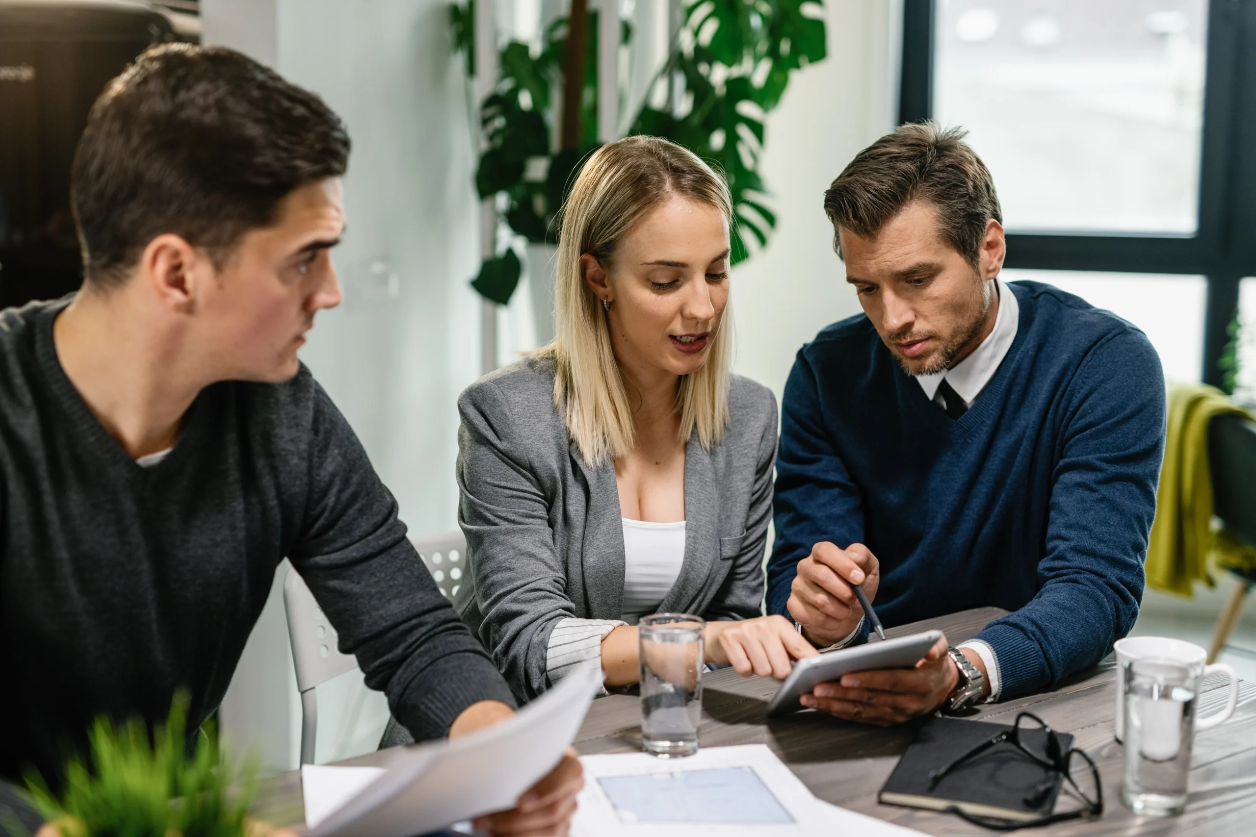 rear-estate-agent-young-couple-going-through-housing-plans-touchpad-while-having-meeting-home-scaled